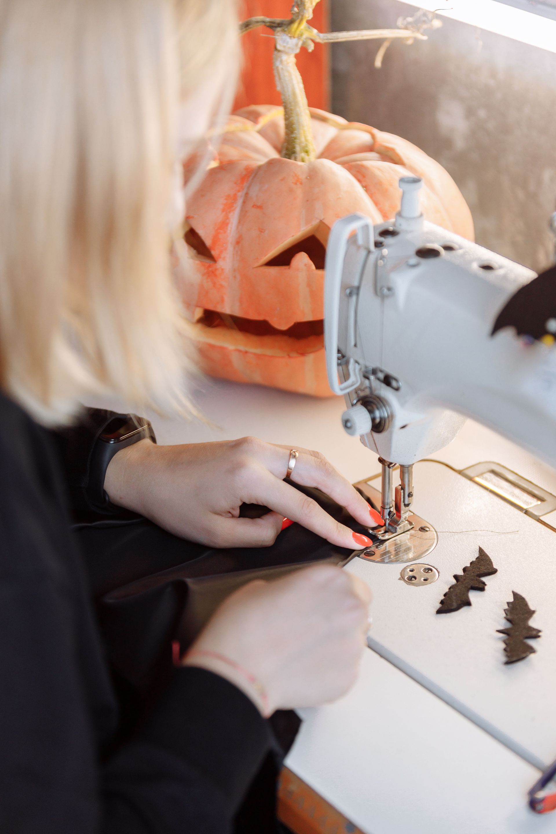 A woman sewing Halloween-themed decorations with a sewing machine beside a carved pumpkin.